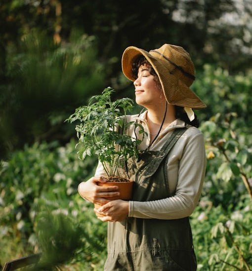 Smiling gardener holding a potted plant while standing in a lush garden, symbolizing the joy and ease of gardening for all skill levels